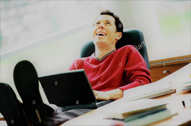 man-sitting-at-desk-with-feet-up-holding-laptop-on-lap-laughing-A5T04P.jpg